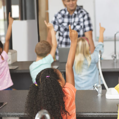 School kids raising hand while teacher asking question